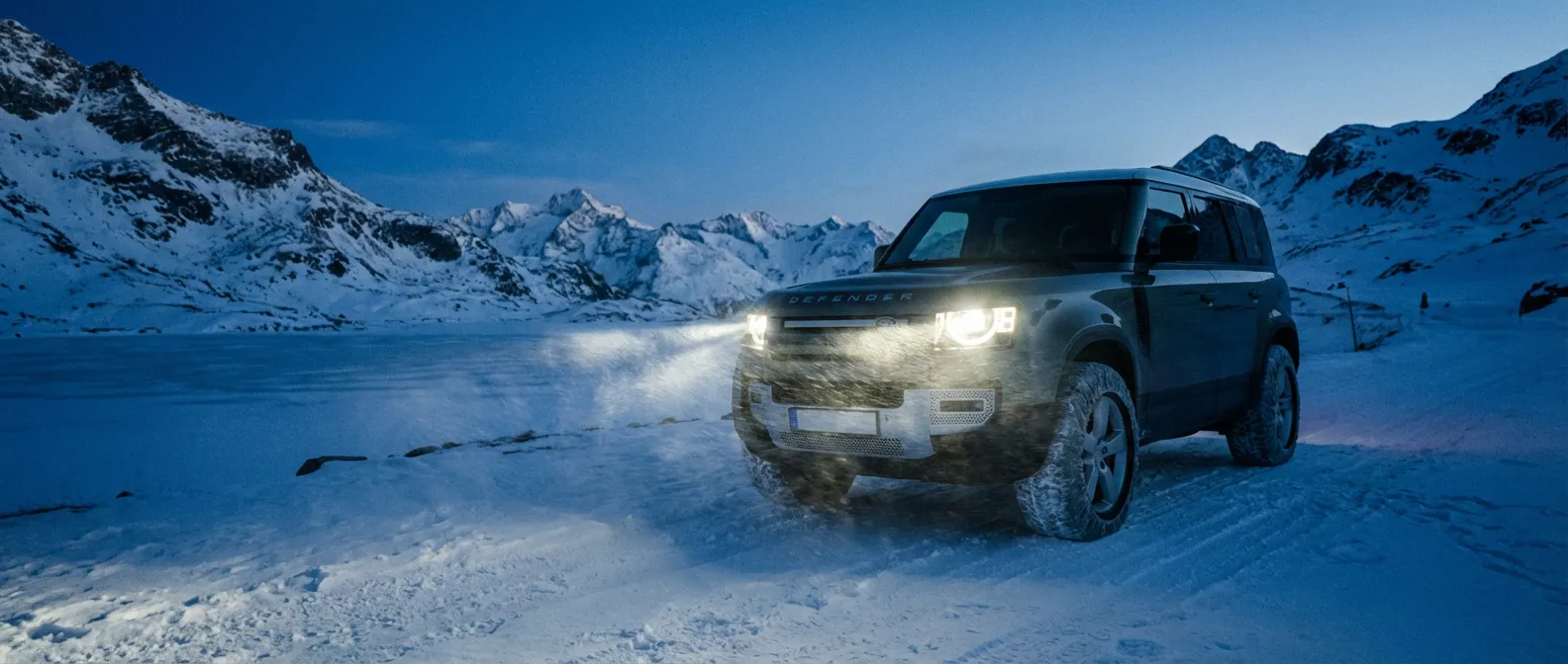 SUV de luxe avec chaussettes à neige sur une route de montagne enneigée des Alpes au crépuscule.