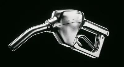 Gros plan iconique d'un pistolet à essence chromé sur fond sombre, symbolisant la consommation.